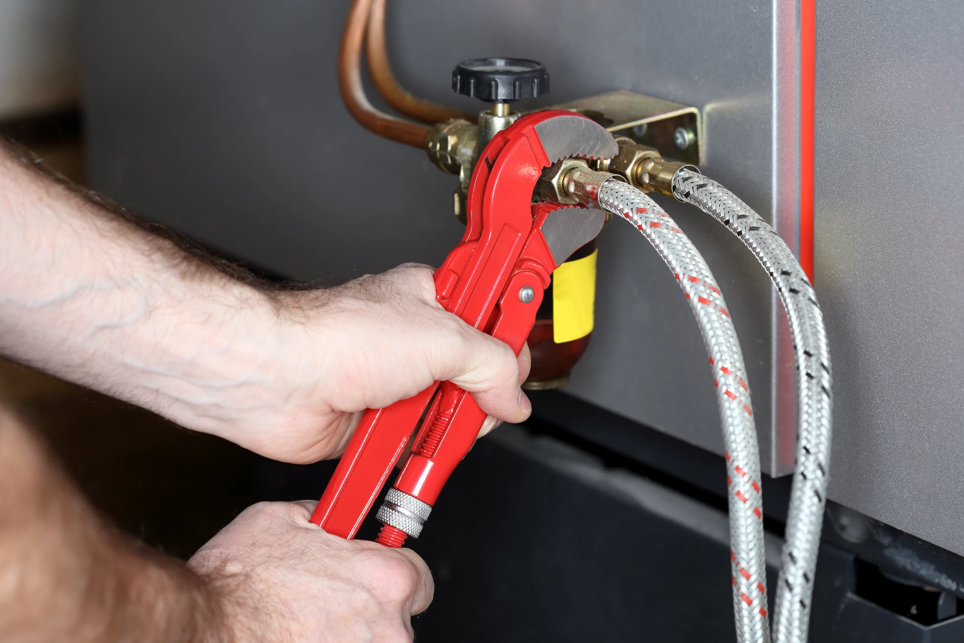 Intervention de plomberie en intérieur, technicien utilisant une clé à sangle rouge sur raccords de plomberie