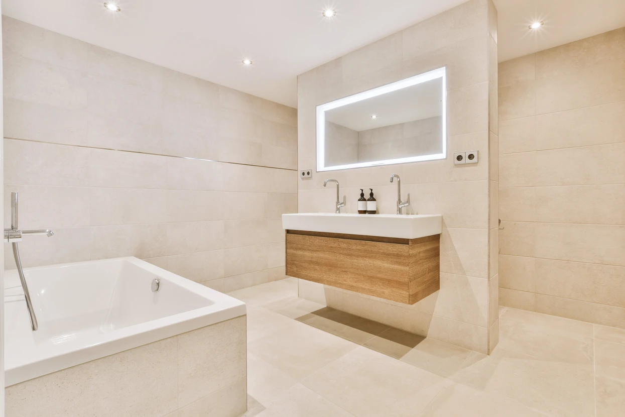 Salle de bain moderne avec baignoire encastrée blanche, meuble vasque suspendu en bois naturel à double robinetterie, miroir rétroéclairé LED