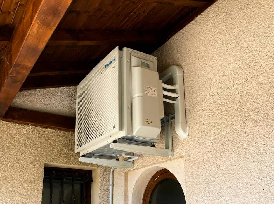 Unité extérieure de climatisation **Daikin** installée en façade d'une maison, fixée sur support mural métallique