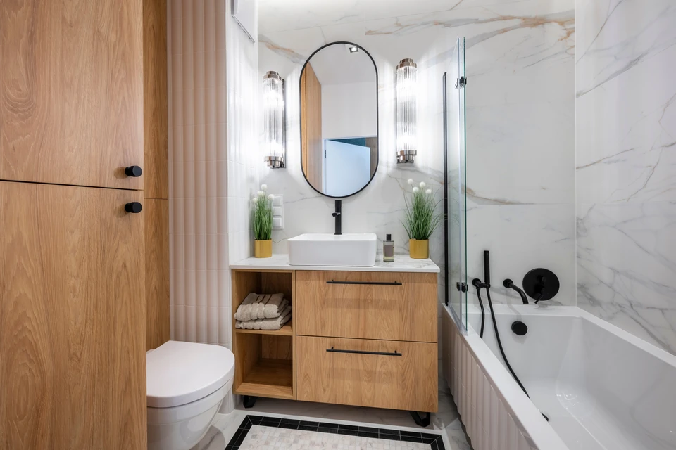 Un plombier professionnel en chemise à carreaux verts et gants bleus répare des toilettes murales dans une salle de bain moderne