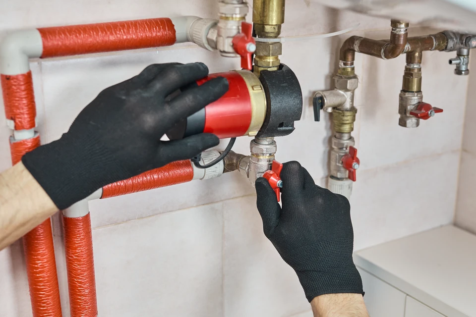 Technicien en combinaison bleue effectuant la maintenance d'une chaudière murale blanche dans un environnement intérieur résidentiel